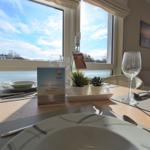 Gestellter Tisch mit Geschirr, Gläsern und Pflanzen vor großem Fenster mit Blick.