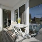 Terrasse mit Tisch, Stühlen und Pflanze. Glasfront führt ins Innere.