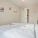 Schlafzimmer mit weißem Bett, Wandbildern und Pflanzen.