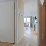 Flur mit Tür zu Schlafzimmer und Blick in Wohnbereich mit Fenster und Pflanze.