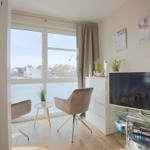 Wohnraum mit TV, Schrank und Sitzgelegenheit vor großem Fenster.