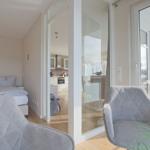 Schlafzimmer mit Blick auf Küche und Balkon. Zwei Sessel und Bett sind sichtbar.