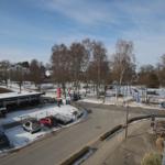 Blick auf verschneite Straße mit Bäumen und Parkplatz.