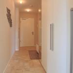 Flur mit Fliesenboden, weißen Schränken und Wanddekoration.