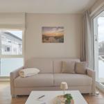 Wohnzimmer mit Sofa, Tisch und Blick auf Balkon.