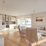 Wohn- und Essbereich mit Küche, Sofa und Stühlen. Holzboden und große Fenster.