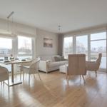 Wohn- und Essbereich mit Holzboden, Sofa, Stühlen und großen Fenstern.