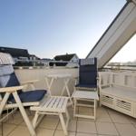 Terrasse mit zwei blauen Sesseln, Tisch und Bank. Blick auf Wohnhäuser und Himmel.