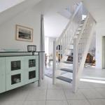 Eingangsbereich mit Treppenhaus und Glasvitrine. Weiße Wände und Fliesenboden.