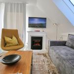 Wohnzimmer mit Sofa, Sessel, Kamin und TV unter Dachschrägen.