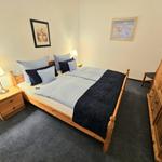 Schlafzimmer mit Holzbett, Nachttisch, Kleiderschrank und Wandbildern.
