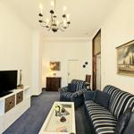 Wohnzimmer mit Sofa, Sessel und Fernseher. Deckenleuchte und Wandbild sichtbar.