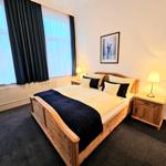 Schlafzimmer mit Holzbett, zwei Nachttischen und großen Fenstern.