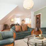 Wohnzimmer mit grünen Sofas, Glas-Tisch und Wandbildern. Küchenbereich im Hintergrund.