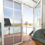 Glasfenster führen auf eine Terrasse mit Blick auf Felder und ein Haus.