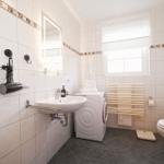 Badezimmer mit Waschmaschine, WC, Spiegel und Fenster.