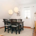 Esszimmer mit Holztisch, Stühlen und zwei Hängelampen. Fenster mit Vorhängen und Küchenzeile.