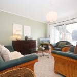 Wohnzimmer mit Sofa, Sessel und Fernseher. Fenster mit Blick nach draußen.