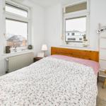 Schlafzimmer mit Bett, zwei Fenstern und Holzregal.