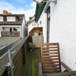 Terrasse mit Holzbank und Pflanzen. Blick auf Nachbarhaus mit Dachterrasse.