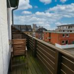 Terrasse mit Holzgeländer und Stuhl. Blick auf Wohnhäuser und Himmel.