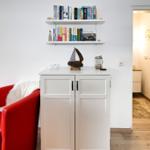 Roter Sessel neben weißem Schrank mit Bücherregal darüber. Blick in angrenzenden Raum.