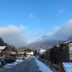 Snow-covered street with houses and mountains in the background.