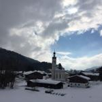 Snow-covered houses and a church in the village under a cloudy sky.