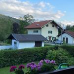 House with garden and mountains in background. Flowers and wooden railing are visible.