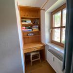 Wooden desk with shelf and stool next to window with view outside.