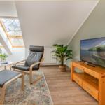 Dachgeschosszimmer mit Sitzgelegenheit, Fernseher und Dachfenstern.