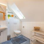 Badezimmer mit Dachschrägen, Waschbecken, Toilette und Holzregal.