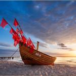 Ein hölzernes Boot mit roten Flaggen liegt am Strand bei Sonnenuntergang.