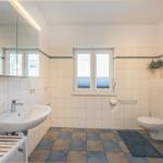 Badezimmer mit Waschbecken, Toilette und Fenster. Fliesenboden und Spiegelschrank.