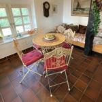 Esszimmer mit Tisch, Stühlen und Fenster. Im Hintergrund Sofa und Wanduhr.