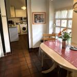 Essbereich mit Tisch, Stühlen und Fenster. Küche mit Waschmaschine sichtbar.