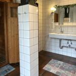 Badezimmer mit Doppelwaschbecken, Spiegel und Sauna im Hintergrund.