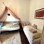 Zimmer mit Doppelbett und Einzelbett, Wandbild mit Rose, Teppich und Kleiderstange.