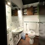 Badezimmer mit Waschbecken, Toilette und Holzregal an der Wand.