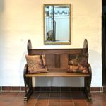 Holzbank mit zwei Kissen unter einem Spiegel an einer Wand.