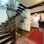 Eingangsbereich mit Treppe und rotem Teppich. Wohnbereich mit Kamin und Holzbalken sichtbar.