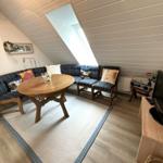 Wohnzimmer mit Sofa, Tisch und Fernseher unter Dachschrägen.