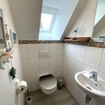 Badezimmer mit Toilette, Waschbecken und Dachfenster. Wandverkleidung mit Mosaikstreifen.