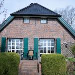 Ein Haus mit Backsteinfassade und grünen Fensterläden. Vor dem Haus steht ein Tisch mit Stühlen.