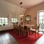 Esszimmer mit Holztisch, Stühlen und rotem Teppich. Fenster und Glastür führen nach draußen.