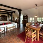 Großes Esszimmer mit Holztisch, Stühlen und Fenstern. Im Hintergrund Wohnbereich mit Holzbalken.