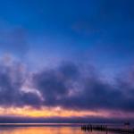 Sonnenuntergang über ruhigem Wasser mit Dock und Boot.
