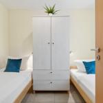Zimmer mit zwei Betten, weißem Schrank und Pflanze.