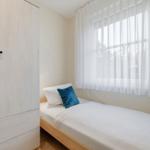 Schlafzimmer mit Bett, Kleiderschrank und Fenster mit Vorhängen.
