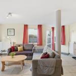 Wohnzimmer mit Sofa, Couchtisch und Fenstern mit roten Vorhängen.